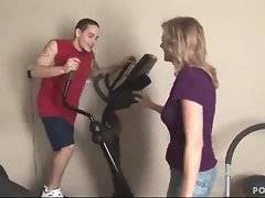 Sexy blonde milf watches cute young guy training in gym.